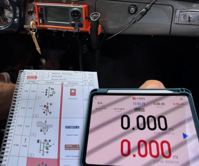 3pRally in funzione su un iPad nella Lancia Aurelia B20 GT del 1954 di Elmer e Sandra Doty, montato accanto a un Terratrip arancione, con il roadbook stampato sulle ginocchia del copilota alla Mille Miglia 2025
